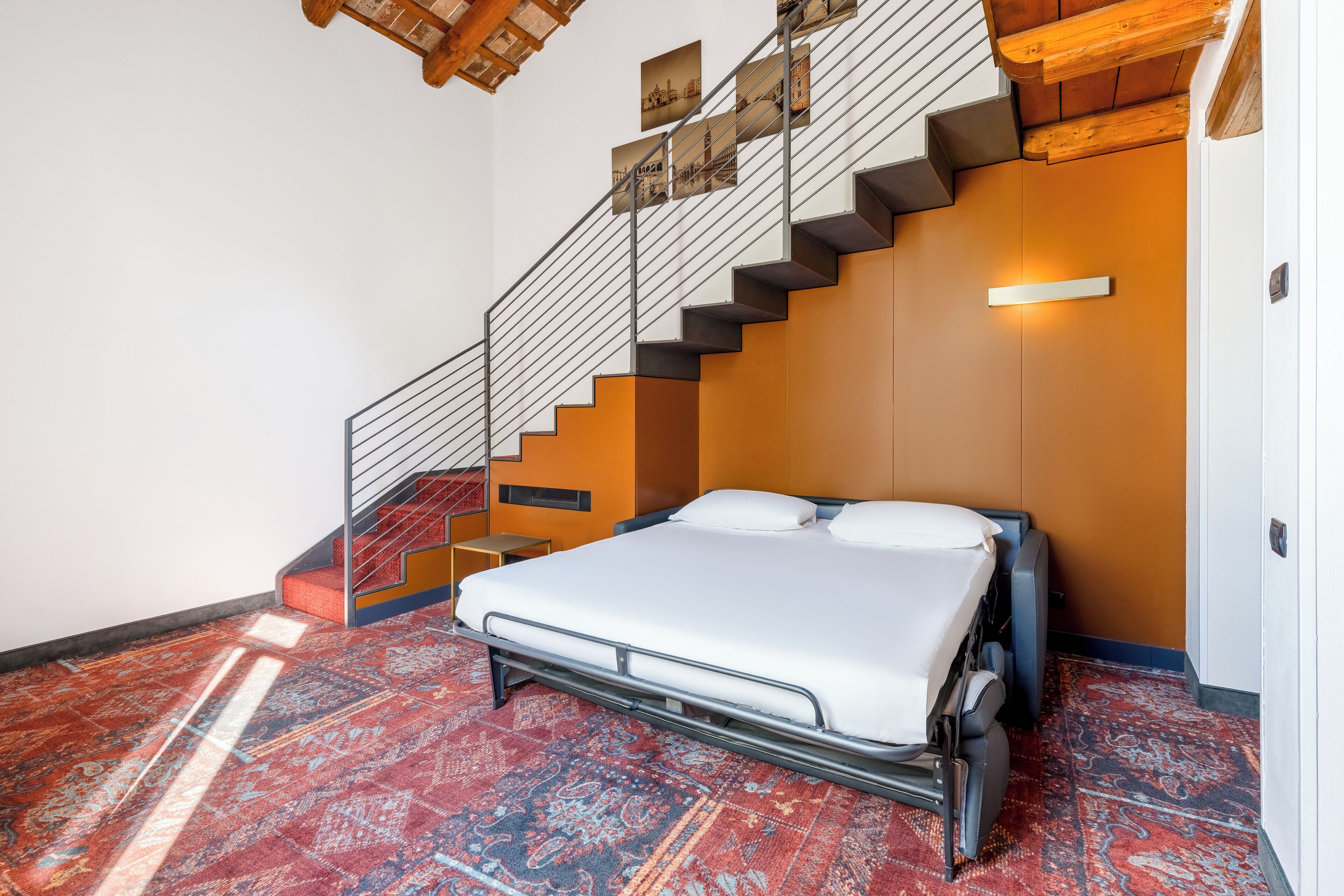 A bedroom with a bed, a staircase, and a patterned carpet.