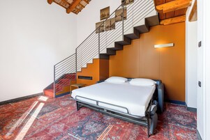 A bedroom with a bed, a staircase, and a patterned carpet.