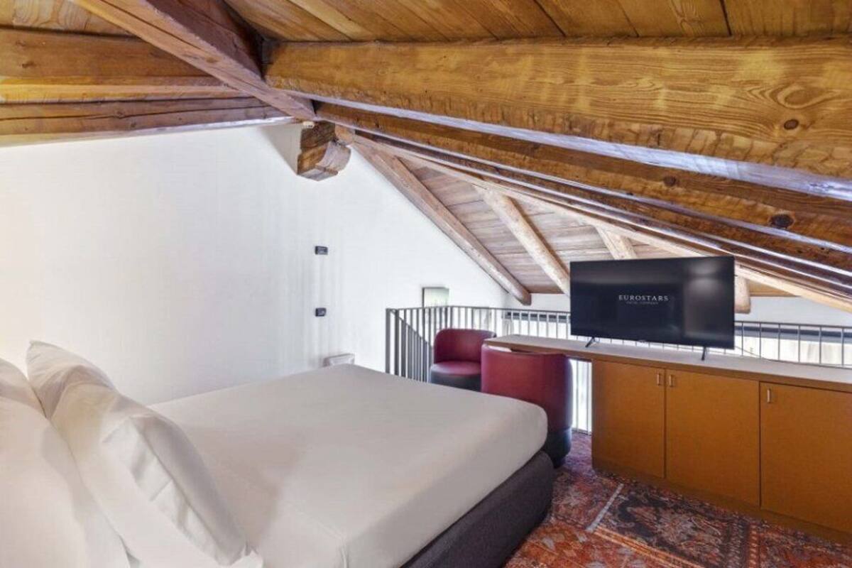 A bedroom with a bed, a television, a red chair, and a wooden ceiling.