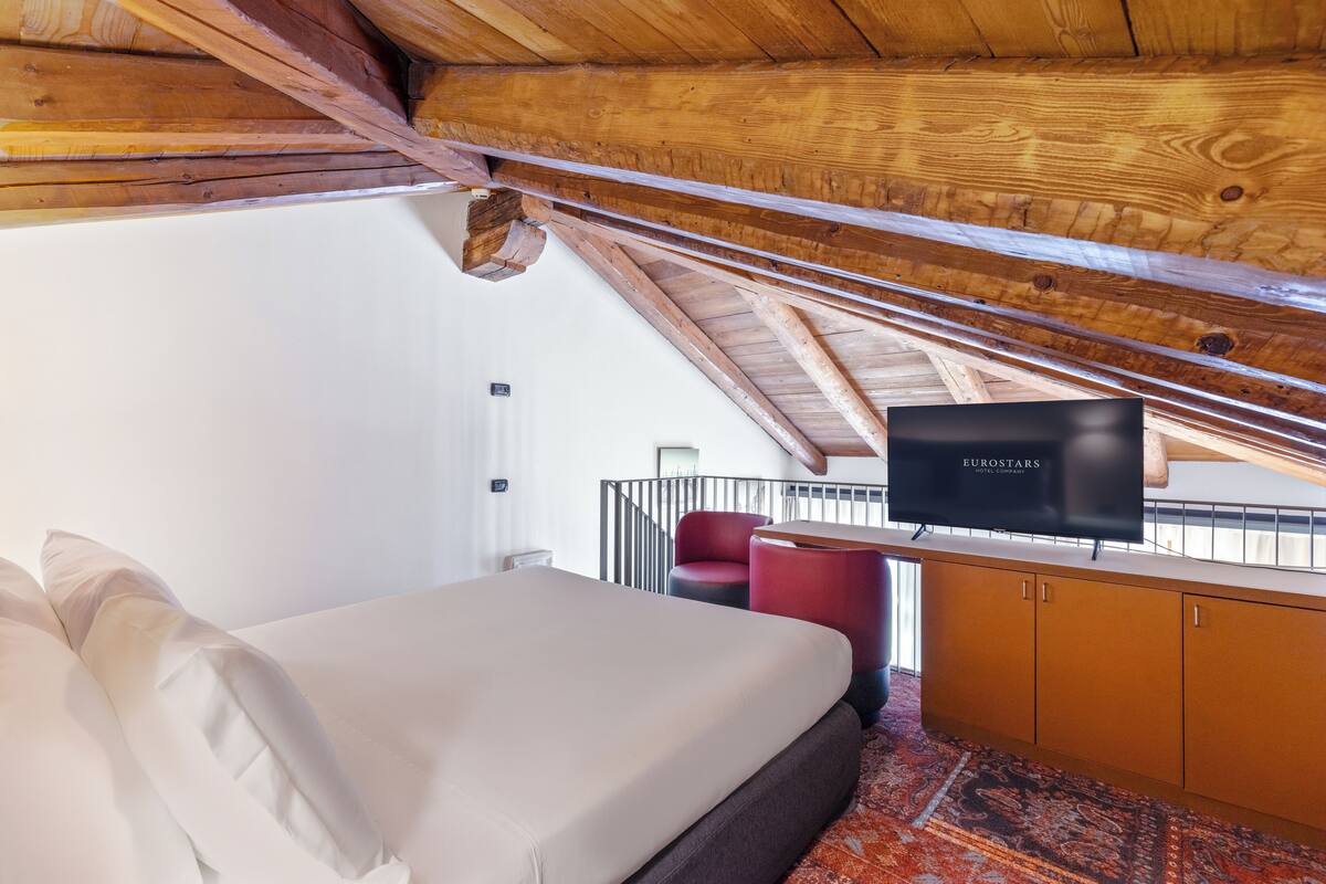 A bedroom with a bed, a television, a red chair, and a wooden ceiling.