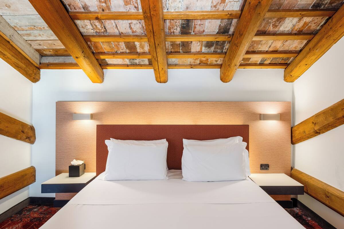 A bedroom with a wooden ceiling, a large bed with white bedding, two bedside tables, and a red accent wall.