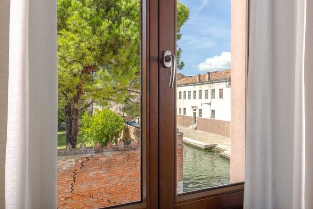 A window with a view of a brick wall, a tree, and a building with a water canal.
