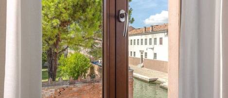 A window with a view of a brick wall, a tree, and a building with a water canal.