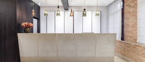 A reception area with a marble counter, hanging pendant lights, and a vase of flowers.