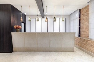 Una zona reception con un bancone in marmo, lampade a sospensione e un vaso di fiori.