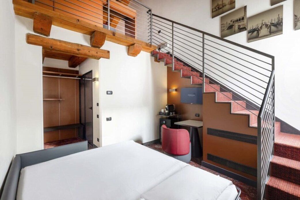 Une chambre d’hôtel comprenant un lit, un bureau, une chaise, un escalier et une porte donnant accès à une salle de bain.
