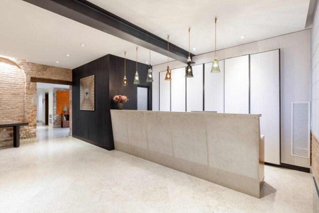 Un área de recepción moderna con mostrador de mármol, lámparas colgantes y pared de ladrillo.