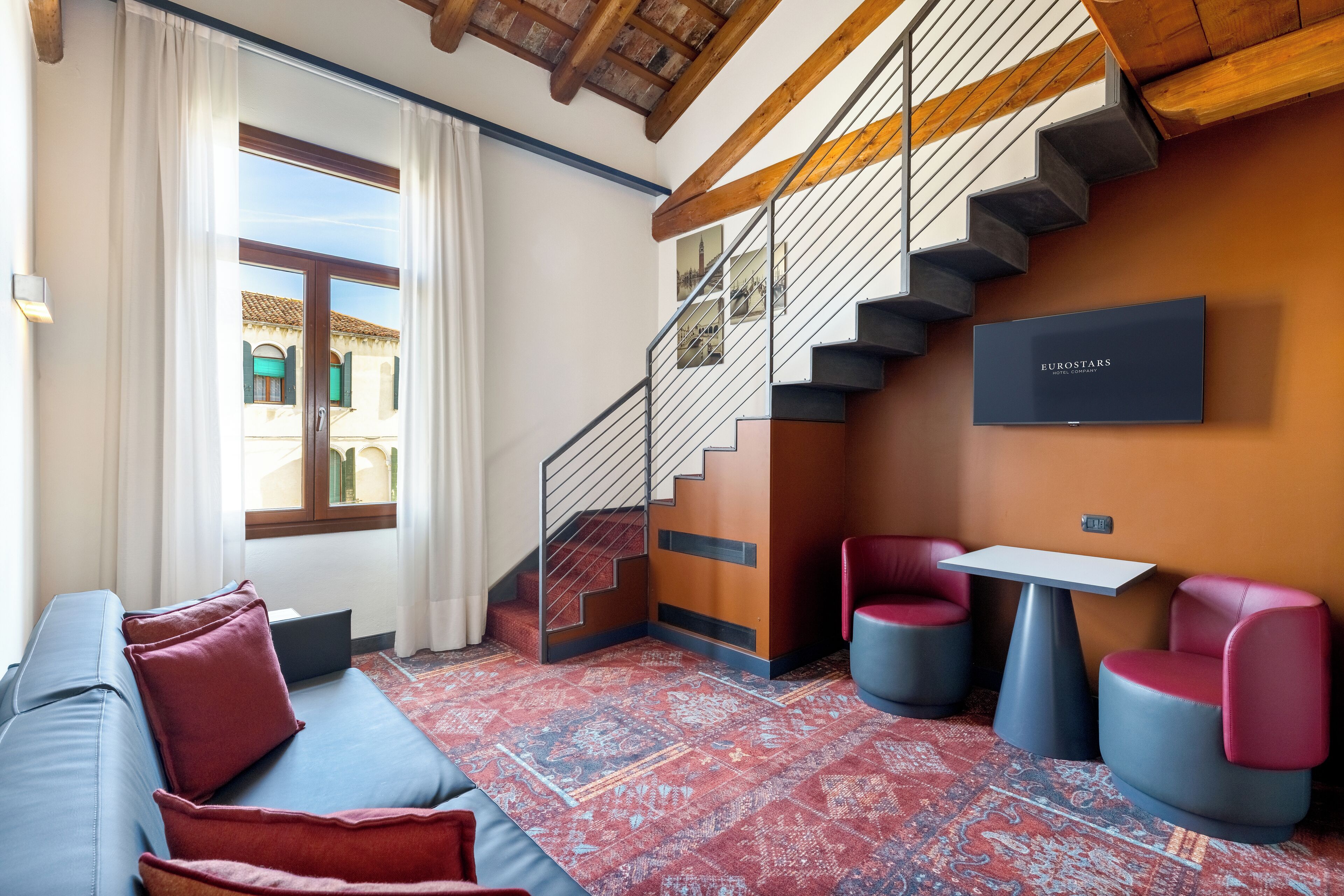 A modern interior with a staircase, a sofa, two chairs, and a table.