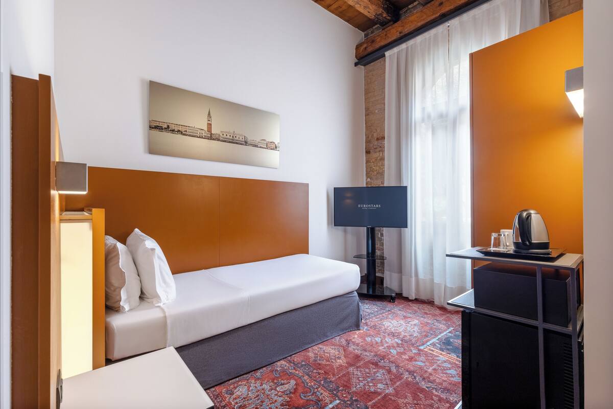 A hotel room with a bed, a television, a coffee maker, and a cityscape painting on the wall.