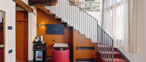 A hotel lobby with a staircase, a red ottoman, a minibar, and framed pictures on the wall.