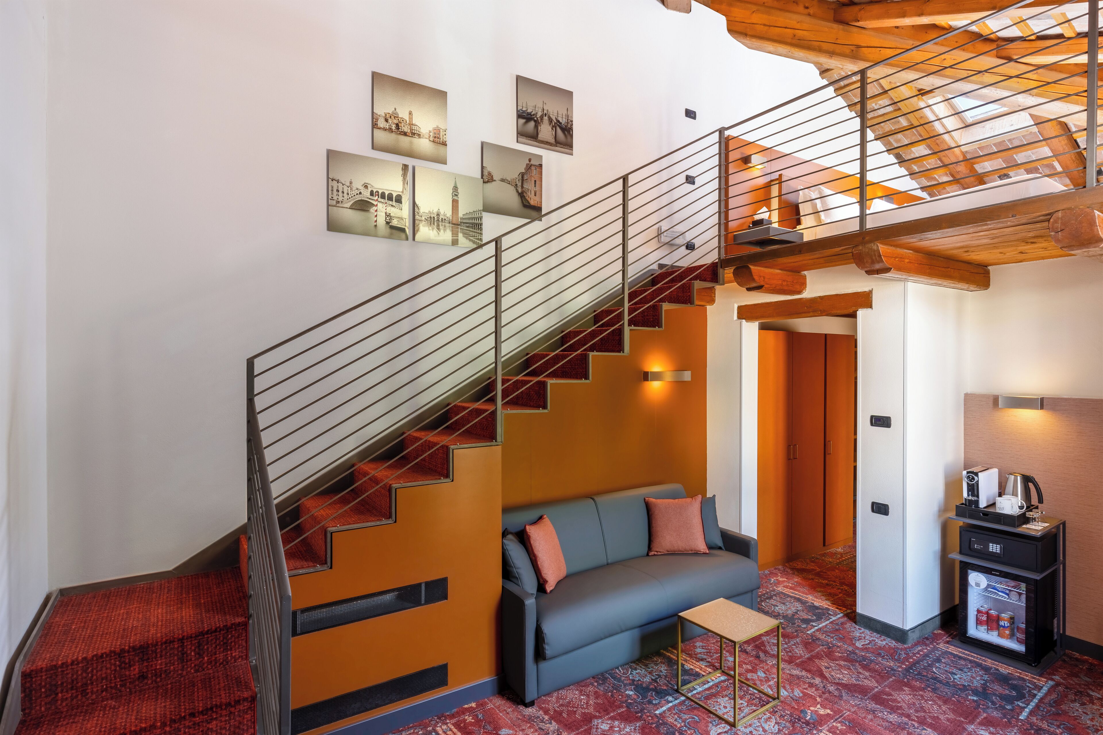 A modern hotel room with a staircase, a sofa, a coffee machine, and a refrigerator.