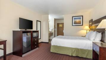 A hotel room with a bed, a television, a desk, and a bathroom visible through an open door.