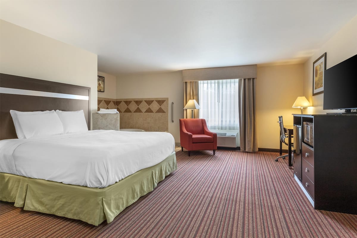 Une chambre d’hôtel avec un grand lit, un bureau, une chaise, une télévision et une fenêtre avec des rideaux.