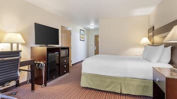 A hotel room with a bed, desk, chair, television, and a small refrigerator.
