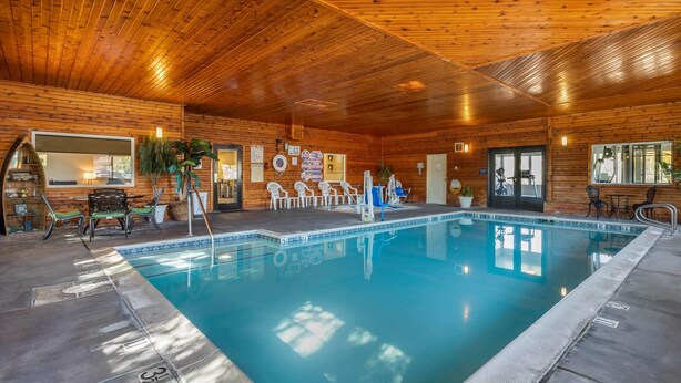 An indoor swimming pool with wooden walls and ceiling, surrounded by lounge chairs and a small seating area.