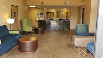 Un hall de hotel con mostrador de recepción, asientos verdes y azules, y suelo de madera.
