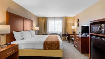 Una habitación de hotel con cama, escritorio, televisor y refrigerador.