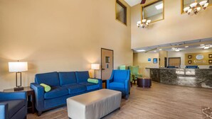 A hotel lobby with a blue sofa, a white ottoman, and a reception desk.