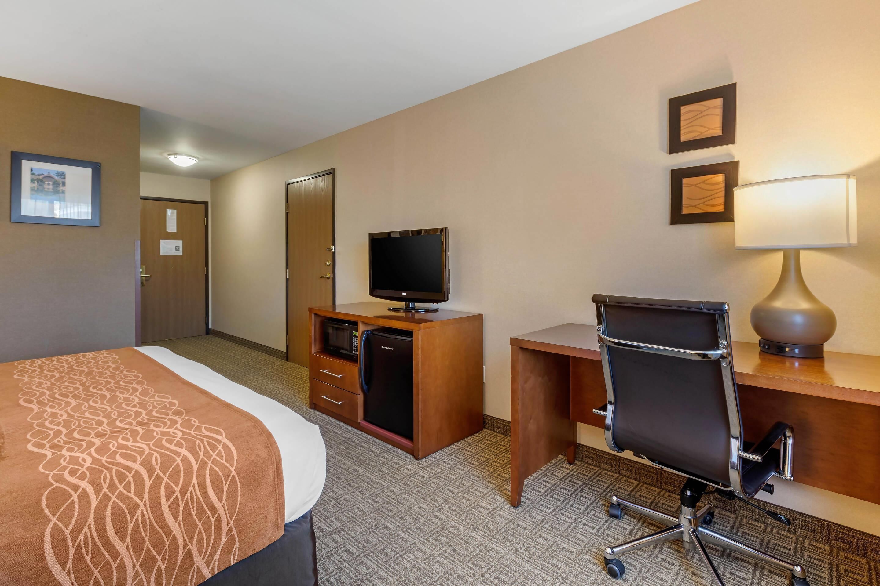 A hotel room with a bed, a desk, a chair, a television, a lamp, and a minibar.