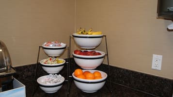 A buffet setup with multiple bowls of fruits and vegetables on a stand.