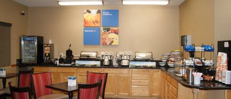 A hotel breakfast area with seating, a coffee machine, and a buffet counter.