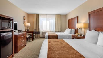 A hotel room with two beds, a desk with a chair, a microwave, a refrigerator, and a window with curtains.