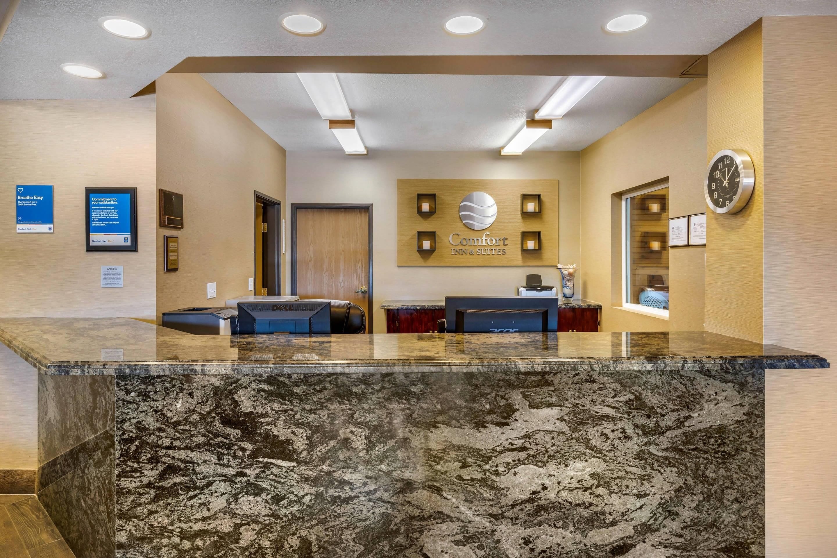 A hotel reception area with a marble counter, a clock, and a sign that reads "Comfort Inn & Suites".