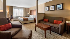 A hotel room with a bed, two sofas, a coffee table, and a desk with a telephone.