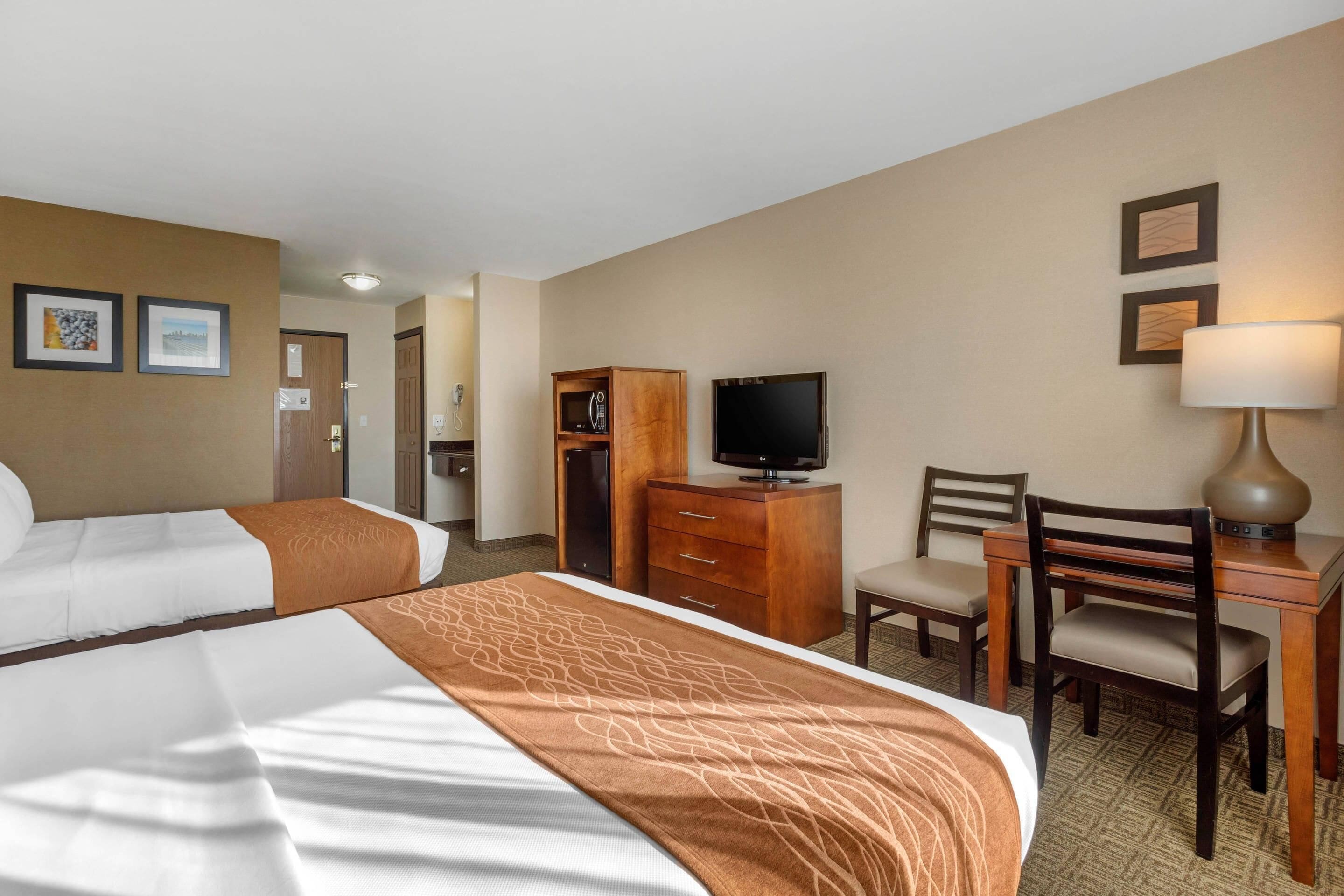 A hotel room with two beds, a desk with a lamp, a television, a chair, and a wardrobe.