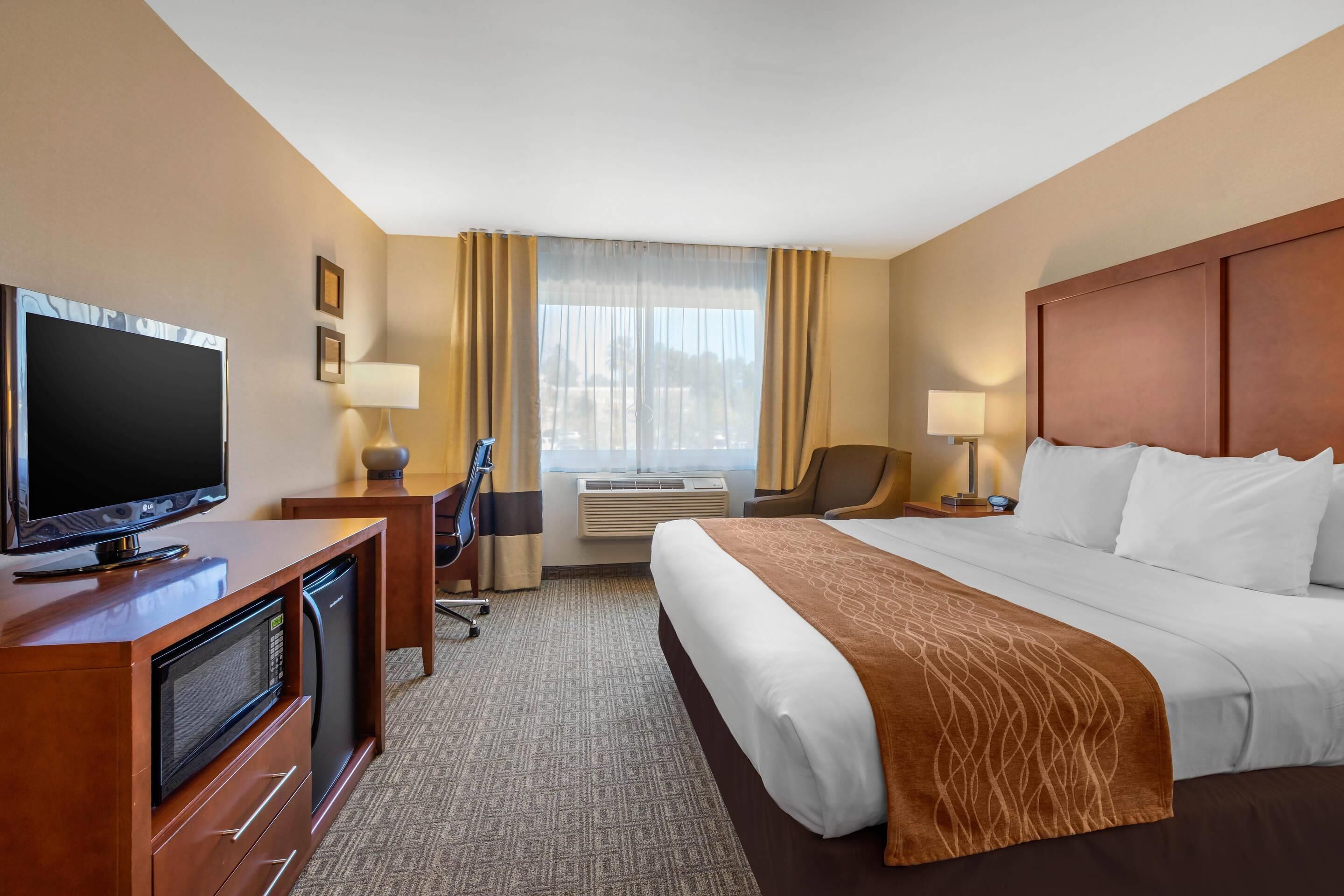 A hotel room with a bed, a desk with a television, a chair, and a window with curtains.