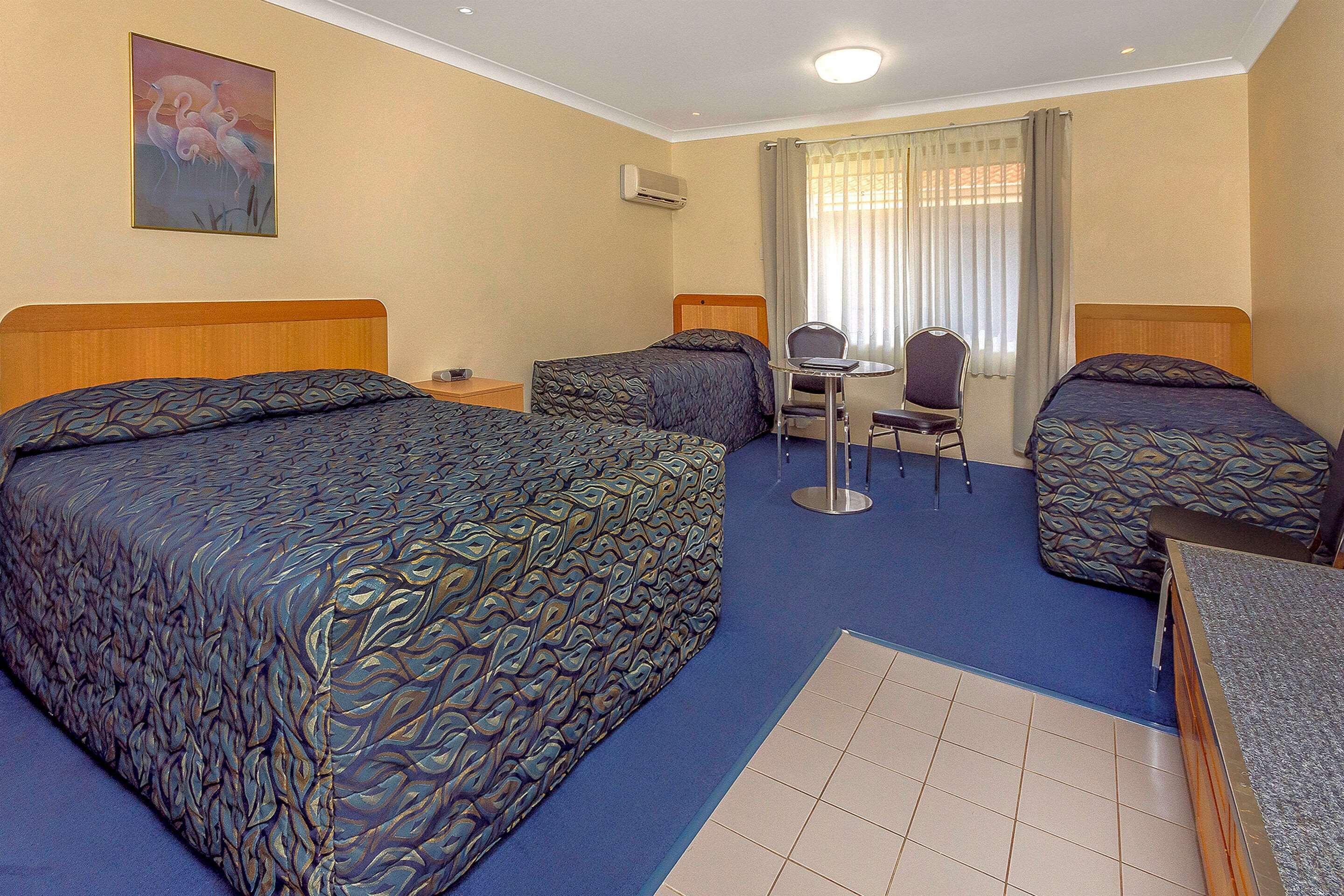 Habitació d'hotel amb tres llits, una taula i una cadira.