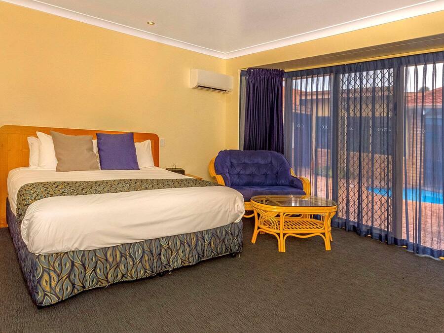 A hotel room with a bed, a chair, a small table, and a view of a pool through sheer curtains.
