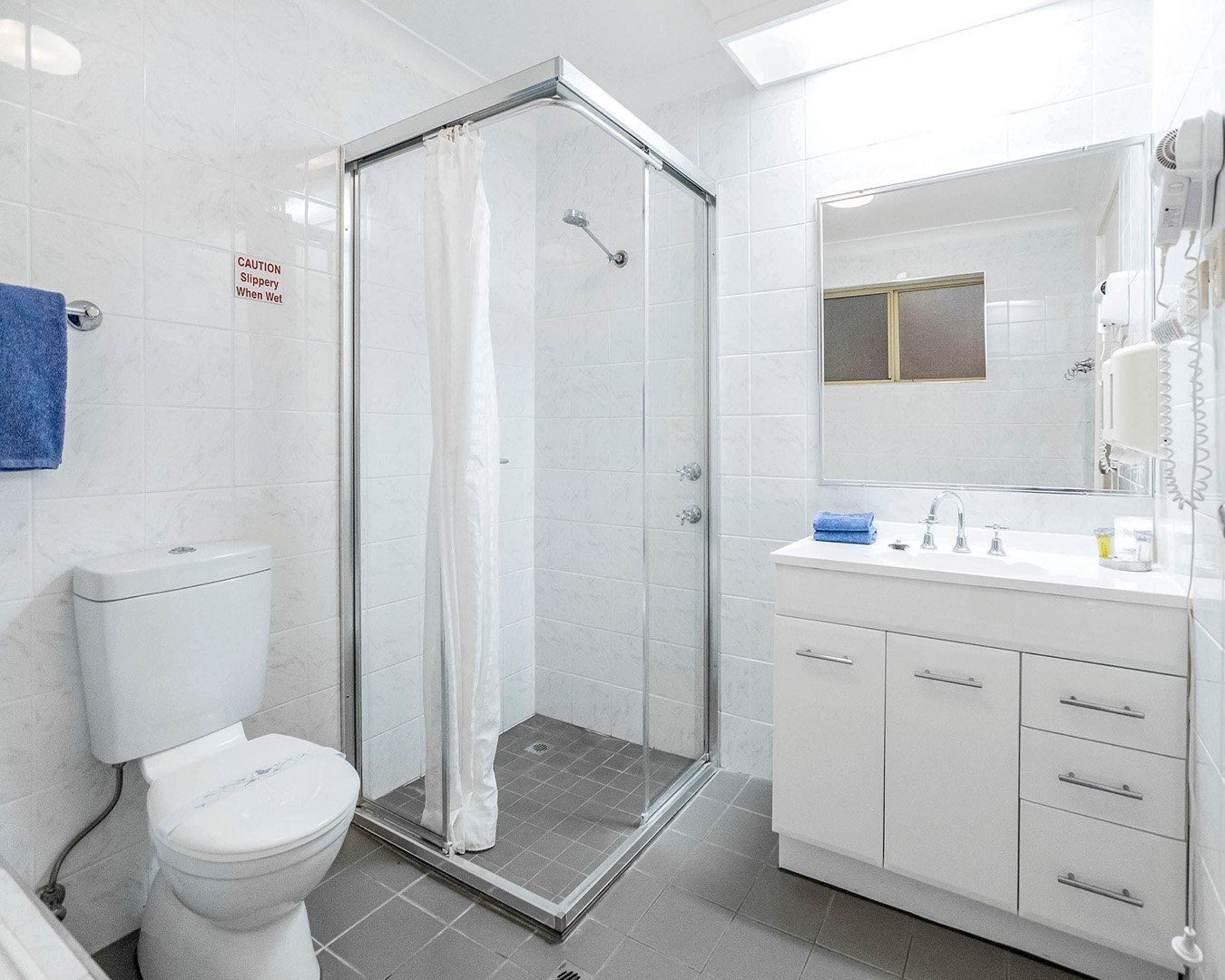 A modern bathroom with a glass shower enclosure, a toilet, a sink with a mirror, and a hairdryer on the wall.