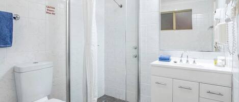 A modern bathroom with a glass shower enclosure, a toilet, a sink with a mirror, and a hairdryer on the wall.