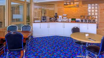 A conference room with a round table, chairs, a coffee station, and a patterned carpet.