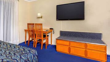 A hotel room with a bed, a desk with a chair, a TV mounted on the wall, and a wooden dresser.