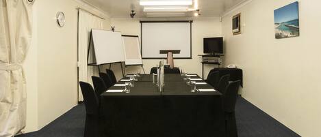 Een vergaderruimte met een lange tafel, stoelen, een projectiescherm, een klok en een schilderij aan de muur.