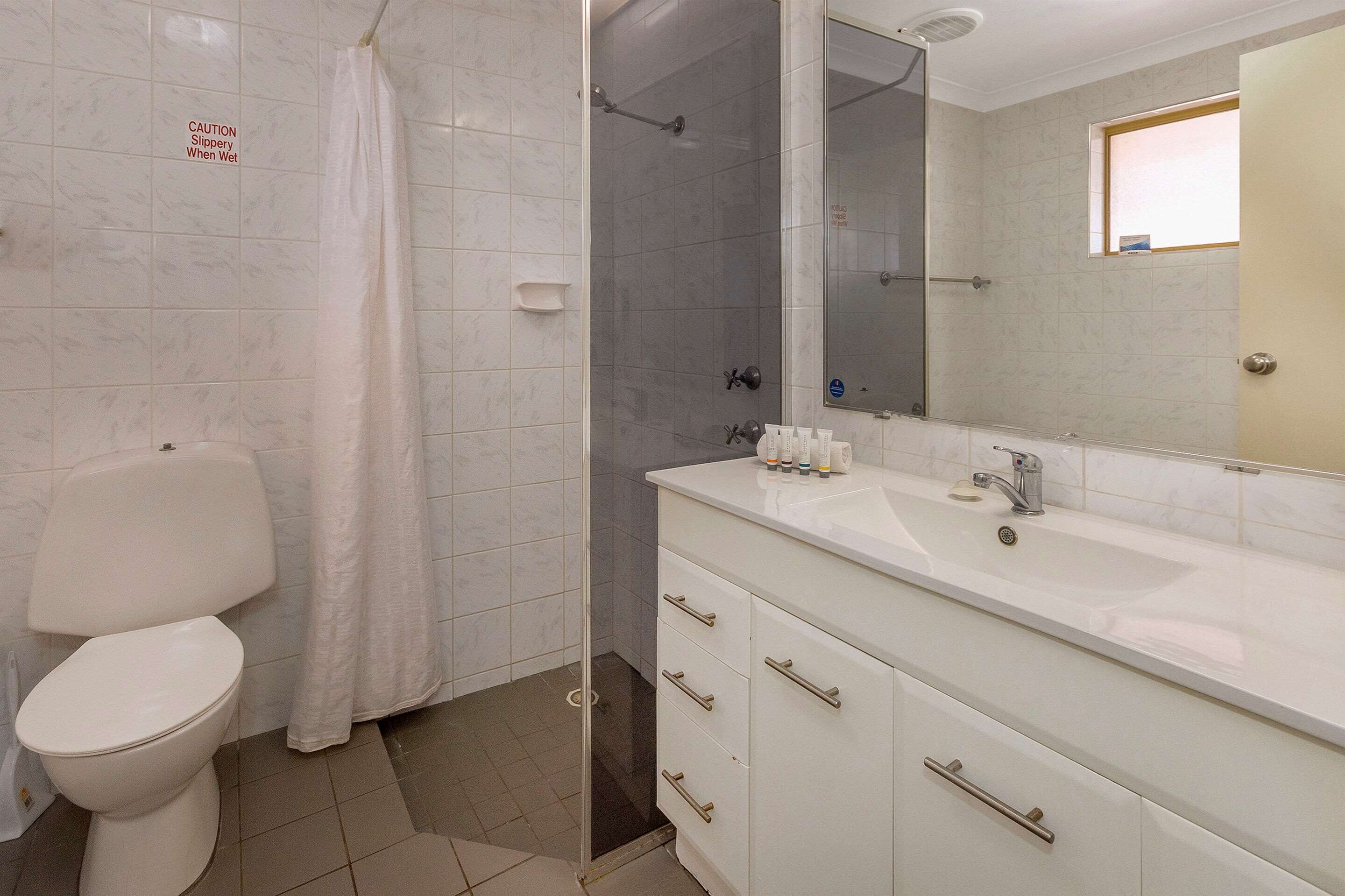 A bathroom with a toilet, shower, sink, and mirror.