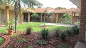 A courtyard with a lawn, palm trees, a swing set, and a brick building. - Comfort Inn Bay Of Isles (Esperance)