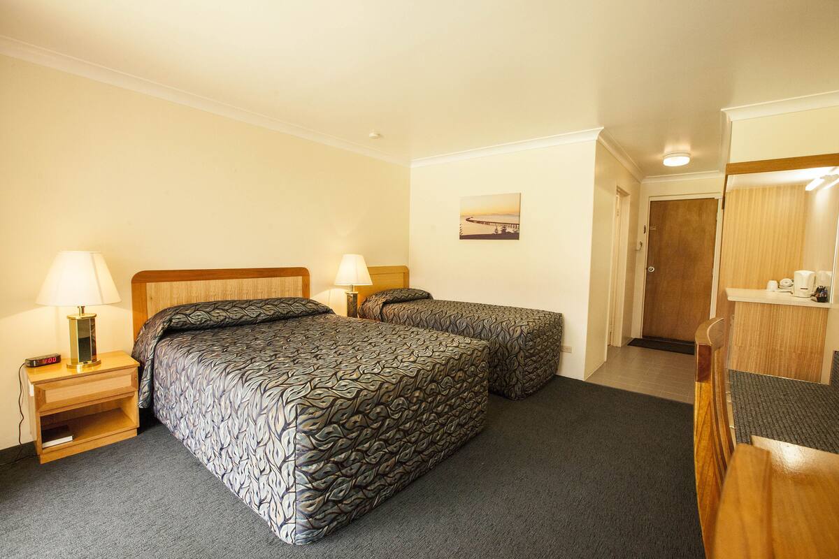 Une chambre d’hôtel avec deux lits, une table de chevet avec une lampe, un tableau au mur et une porte donnant sur une autre pièce.