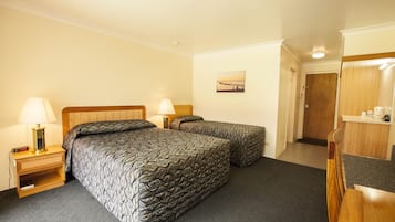 Ein Hotelzimmer mit zwei Betten, einem Nachttisch mit Lampe, einem Gemälde an der Wand und einer Tür zu einem anderen Raum.