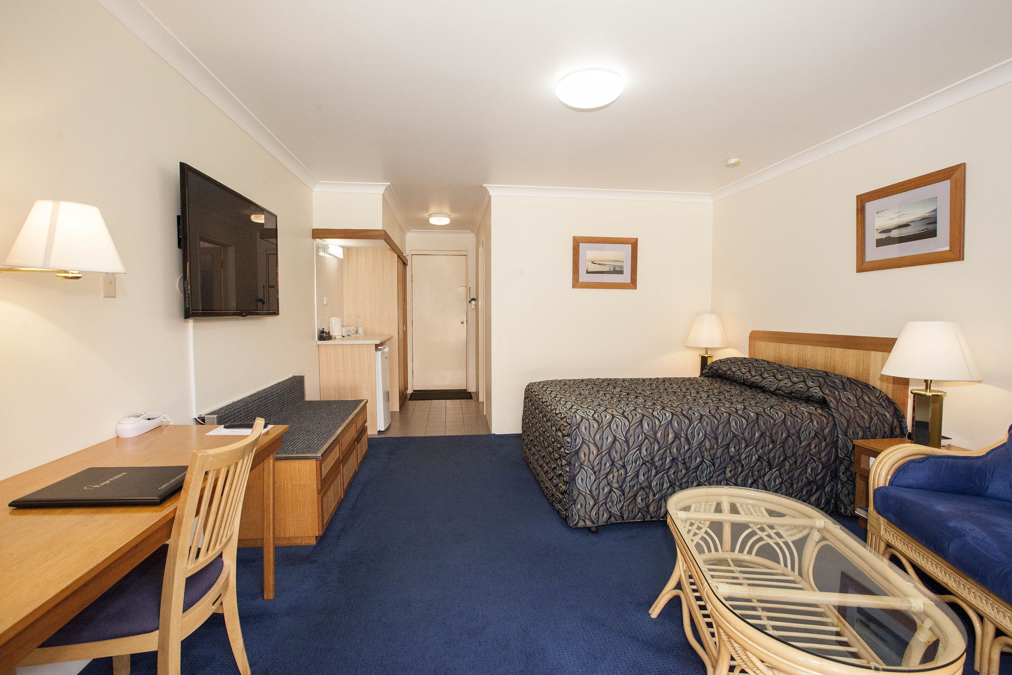 Une chambre d’hôtel avec un lit, un bureau, une chaise, une télévision et une salle de bain visible à travers une porte ouverte.