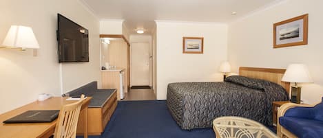 Une chambre d’hôtel avec un lit, un bureau, une chaise, une télévision et une salle de bain visible à travers une porte ouverte.