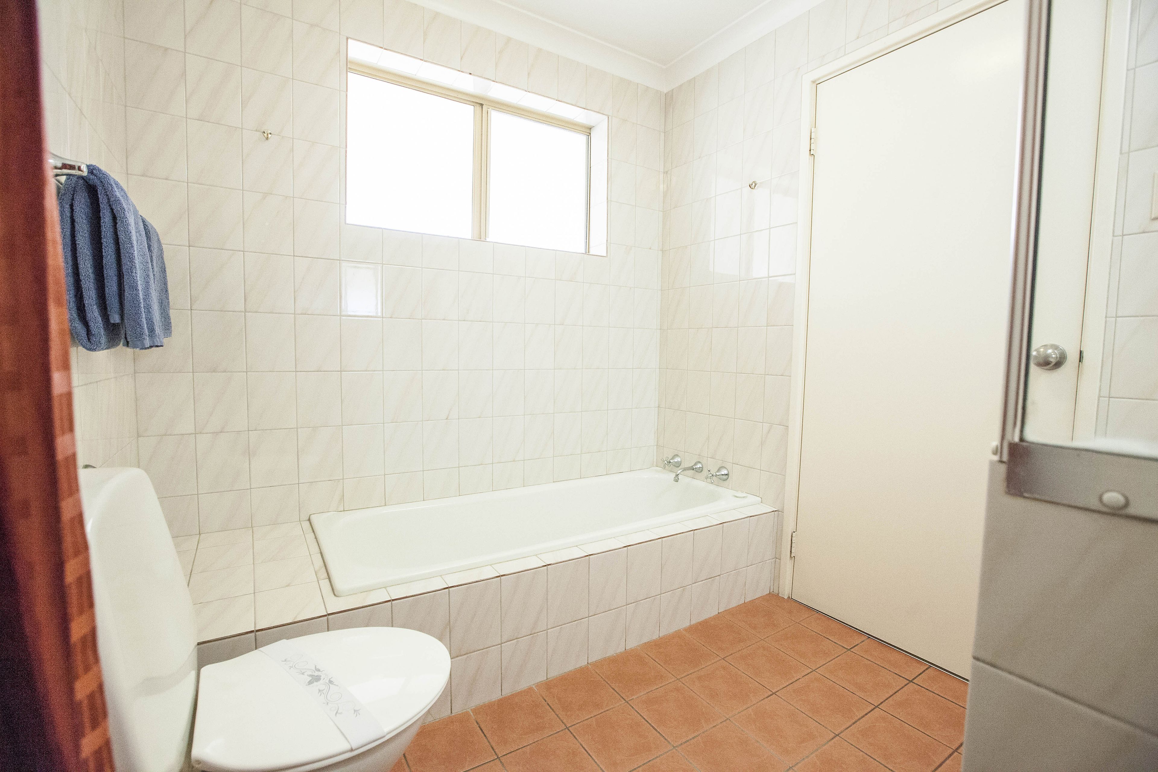 A bathroom with a white bathtub, a toilet, and a window.