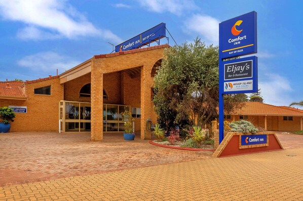 Un hotel Comfort Inn Bay of Isles con fachada de ladrillo, entrada de vidrio y señalización para Eljay's Bar & Restaurant y Woody Island Eco Tours.