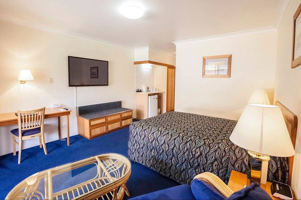 Une chambre d’hôtel équipée d’un lit, d’un bureau, d’une chaise, d’une petite table, d’une lampe et d’un téléviseur.