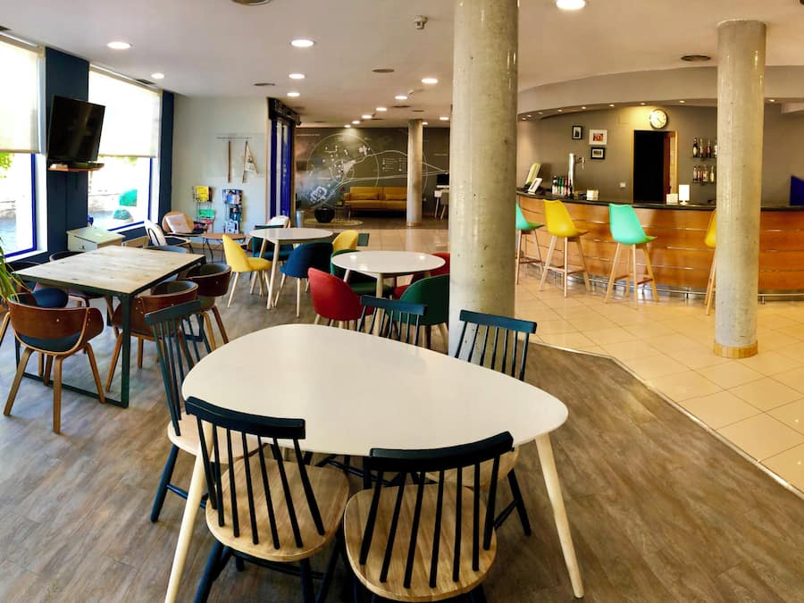 Un vestíbulo de hotel con mostrador de recepción, zona de estar con mesas y sillas, y un amplio ventanal con vistas.