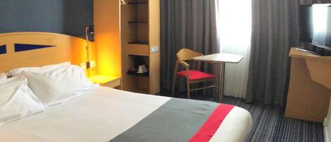 Una habitación de hotel con cama, escritorio, silla, televisor y armario.