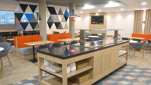 A modern restaurant with a central bar, orange seating, and a geometric patterned floor. - Holiday Inn Express Madrid-San Sebastian de los Reyes by IHG (San Sebastian de los Reyes)