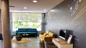 Un espace de détente moderne comprenant un canapé, des fauteuils, un bureau et une grande fenêtre donnant sur un paysage verdoyant.